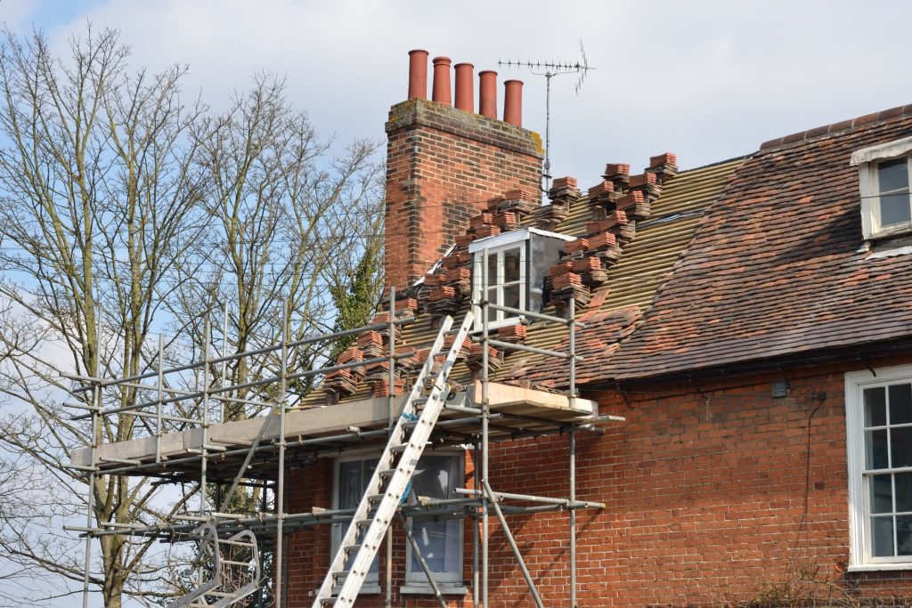 Scaffolding and ladder positioned beside a partially repaired roof with missing tiles, illustrating emergency roof repairs after storm damage.