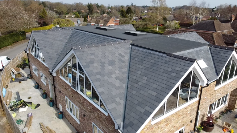 Aerial view of a modern residential roof featuring slate tiles, multiple gables, and large windows, showcasing roofing design and construction relevant to homeowner maintenance and repair tips.