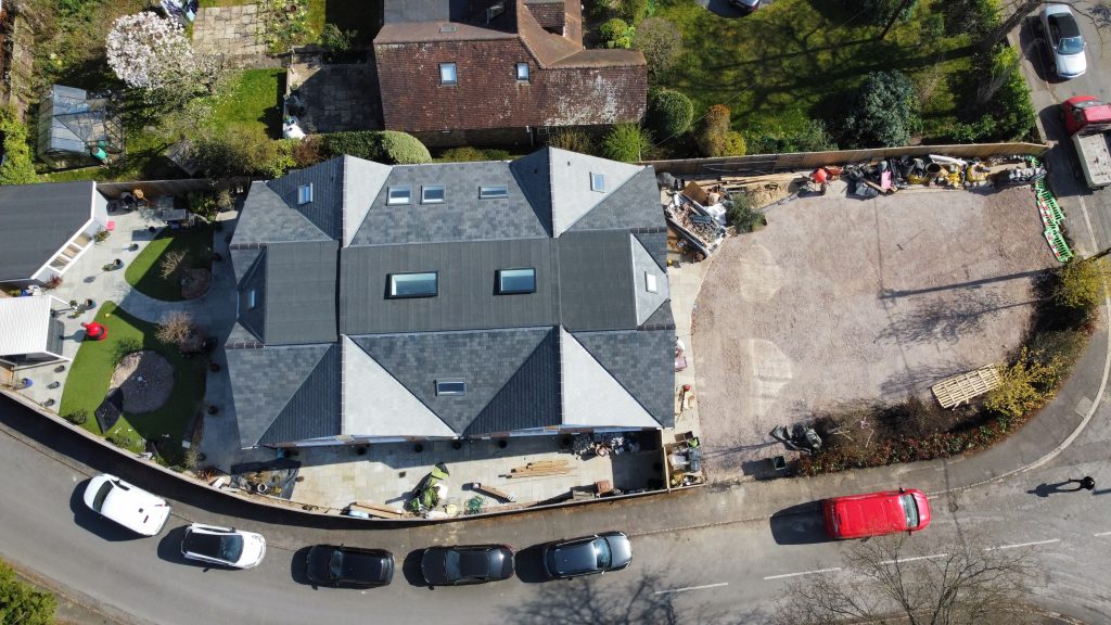 Aerial view of a residential property featuring a newly installed slate roof, surrounded by landscaped gardens and construction materials, relevant to roof repair and maintenance services offered by CRS Roofing.