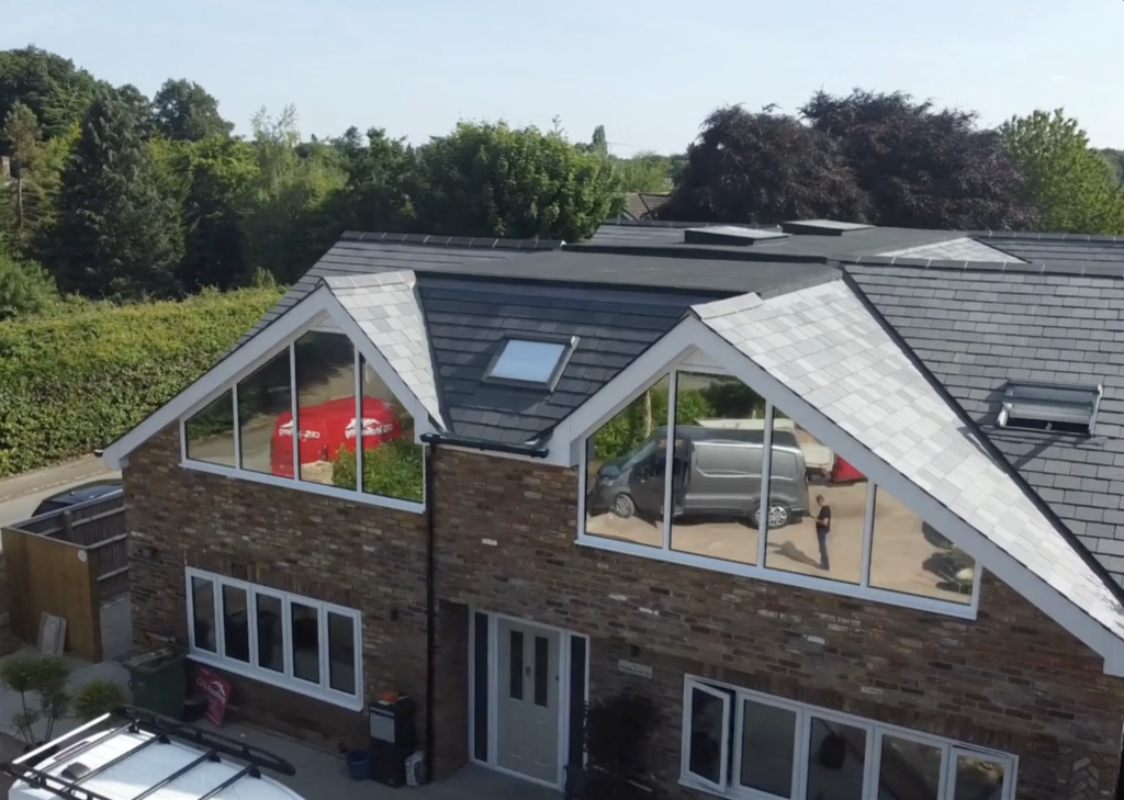 Modern home with sloped roof, large windows reflecting surrounding greenery and vehicles, showcasing potential roofing solutions and maintenance after storm damage.